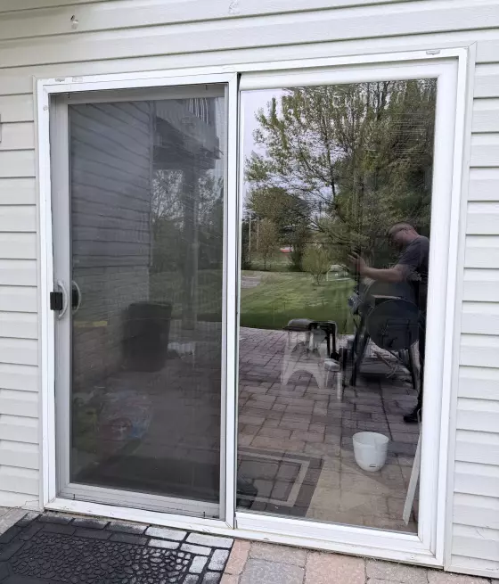 Exterior view of a sliding glass door with white siding and a doormat