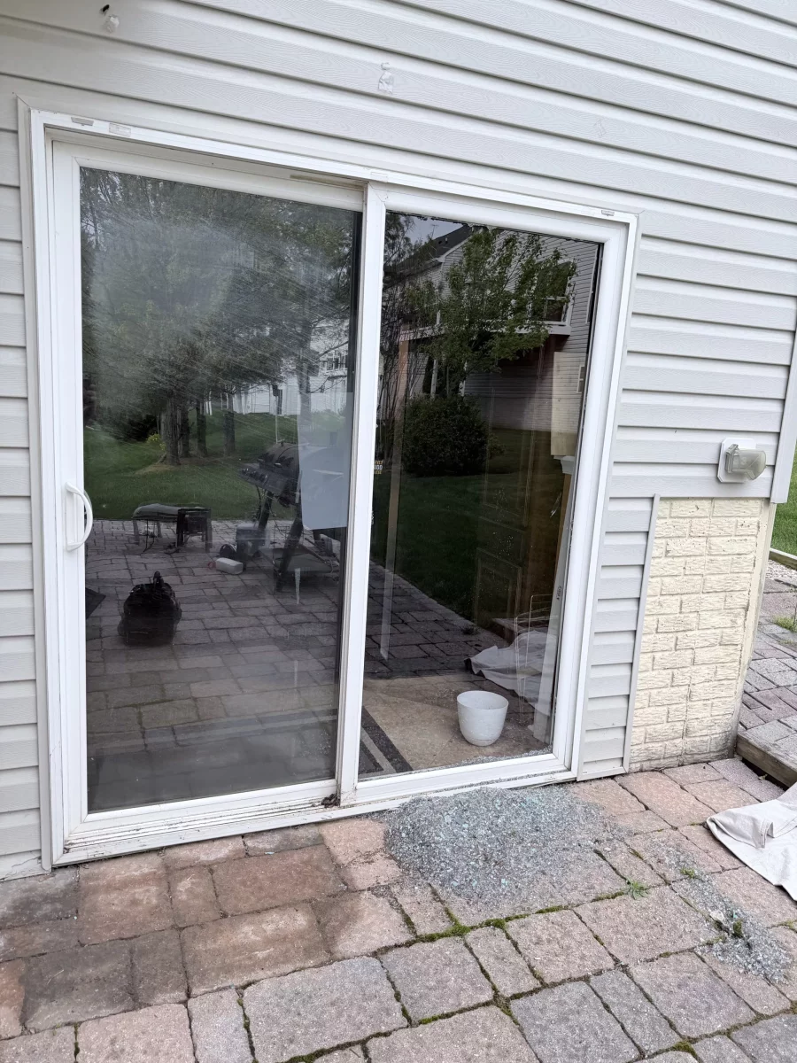 Sliding glass door with broken glass on patio outside residential home