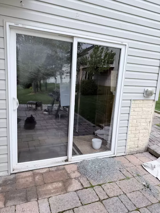 Sliding glass door with broken glass on patio outside residential home