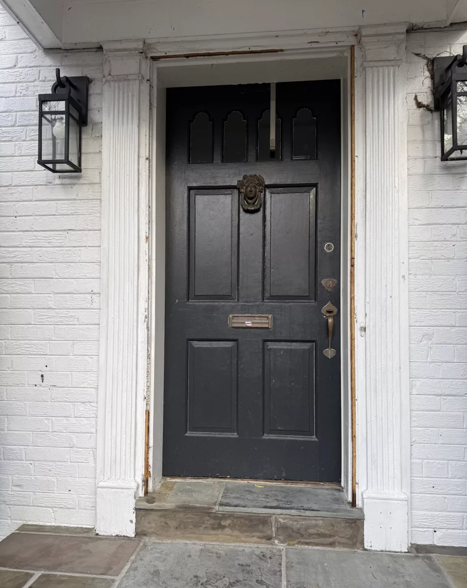Exterior view of a black front door with visible damage and worn trim.