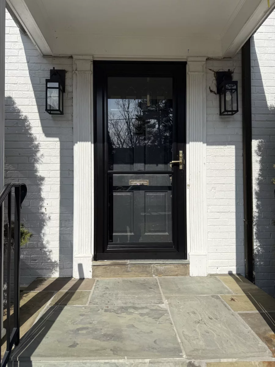 Black exterior door with glass panel and white brick facade