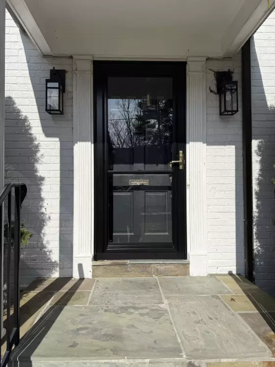 Black exterior door with glass panel and white brick facade
