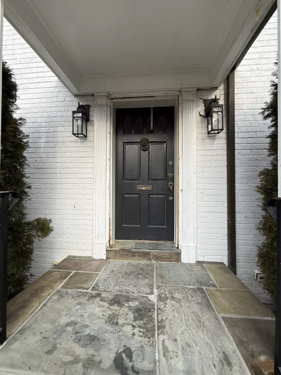 Exterior view of a black entry door with visible damage and white brick facade