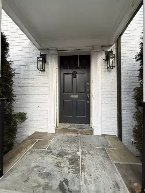 Exterior view of a black entry door with visible damage and white brick facade