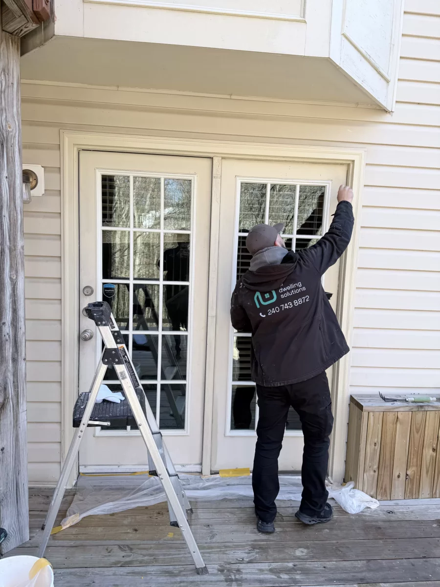 Person working on exterior french doors with ladder and drop cloth