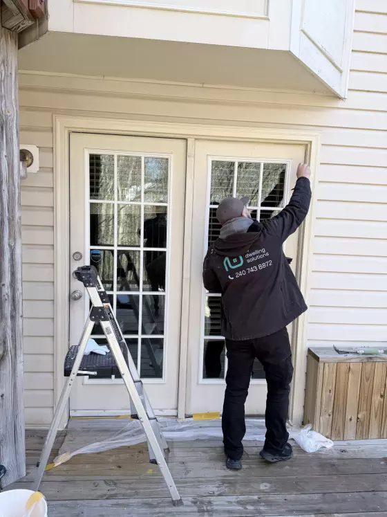 Person working on exterior french doors with ladder and drop cloth