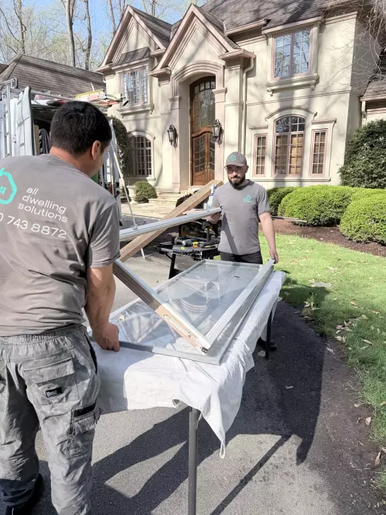 Two workers handling a window sash outside a residential house