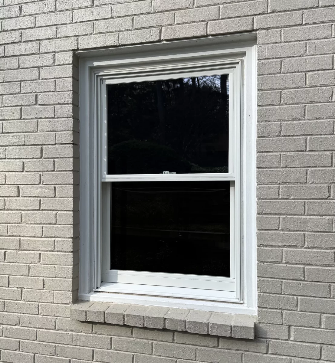 White framed window installed in painted brick exterior wall