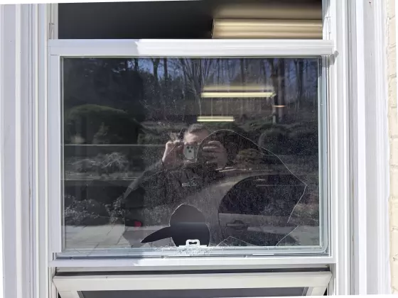 Broken glass in residential window with person reflected