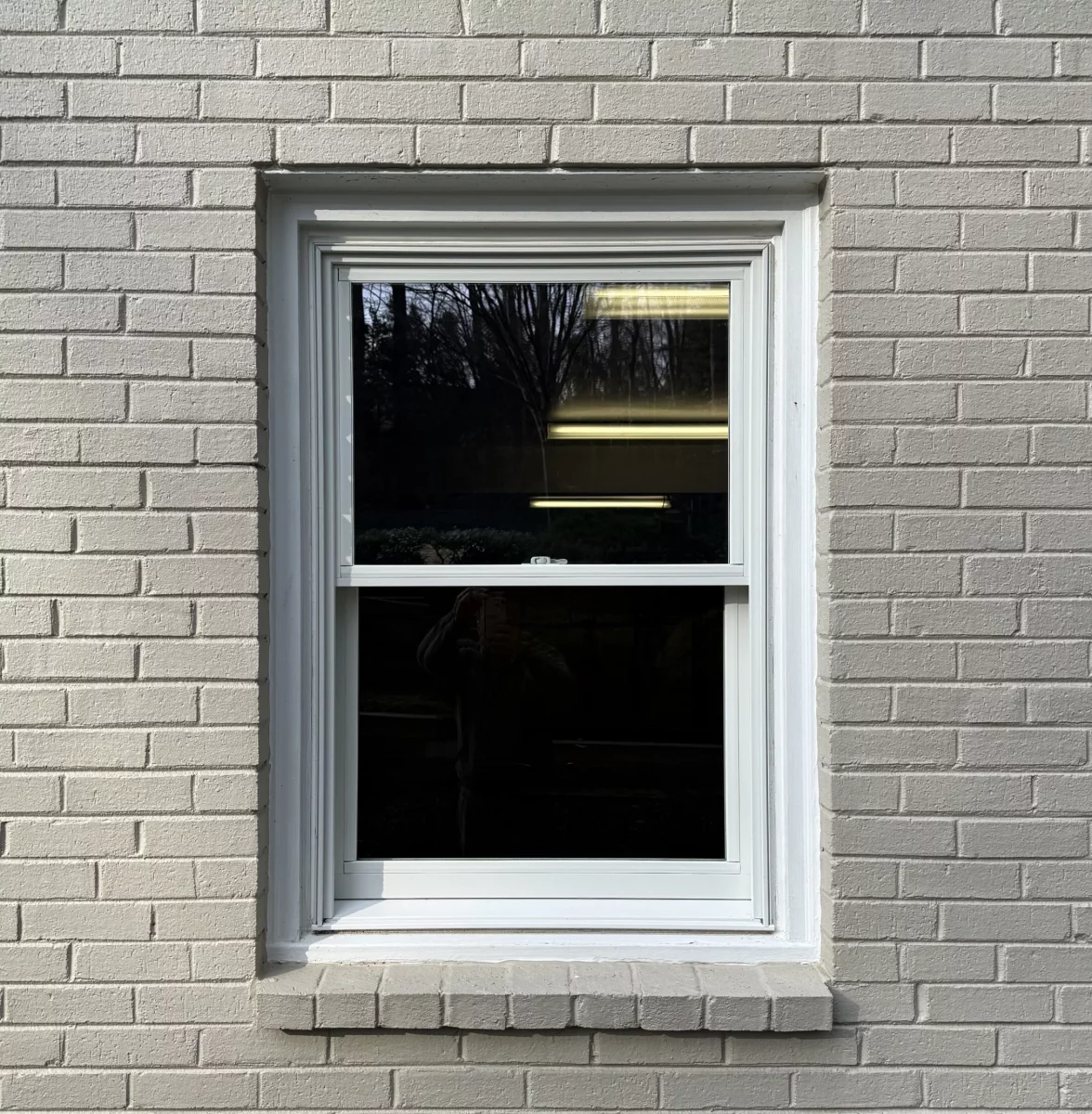 White framed window installed in painted brick exterior wall