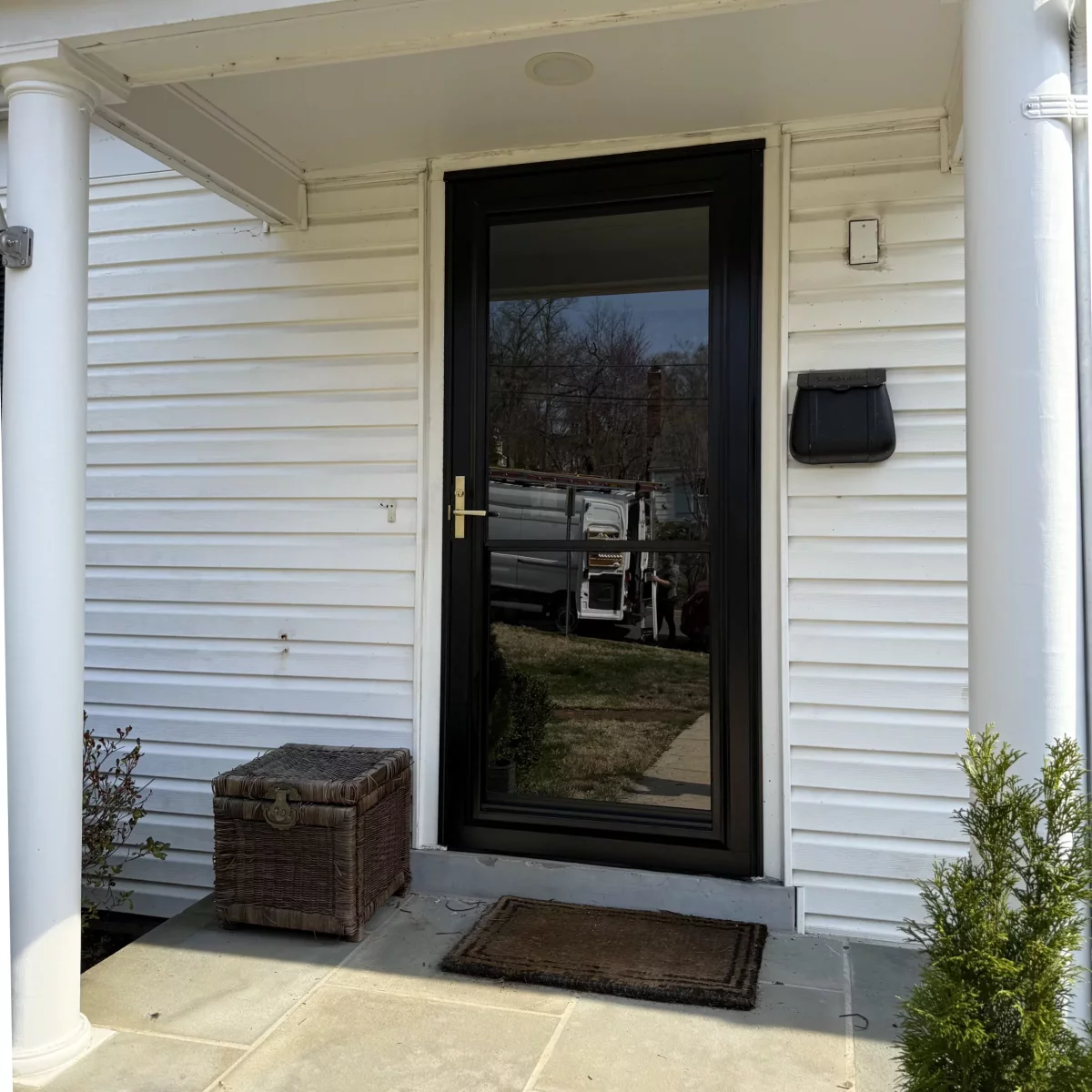 Black storm door installed on white house exterior with columns