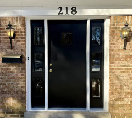 Black entry door with glass panels and brick exterior