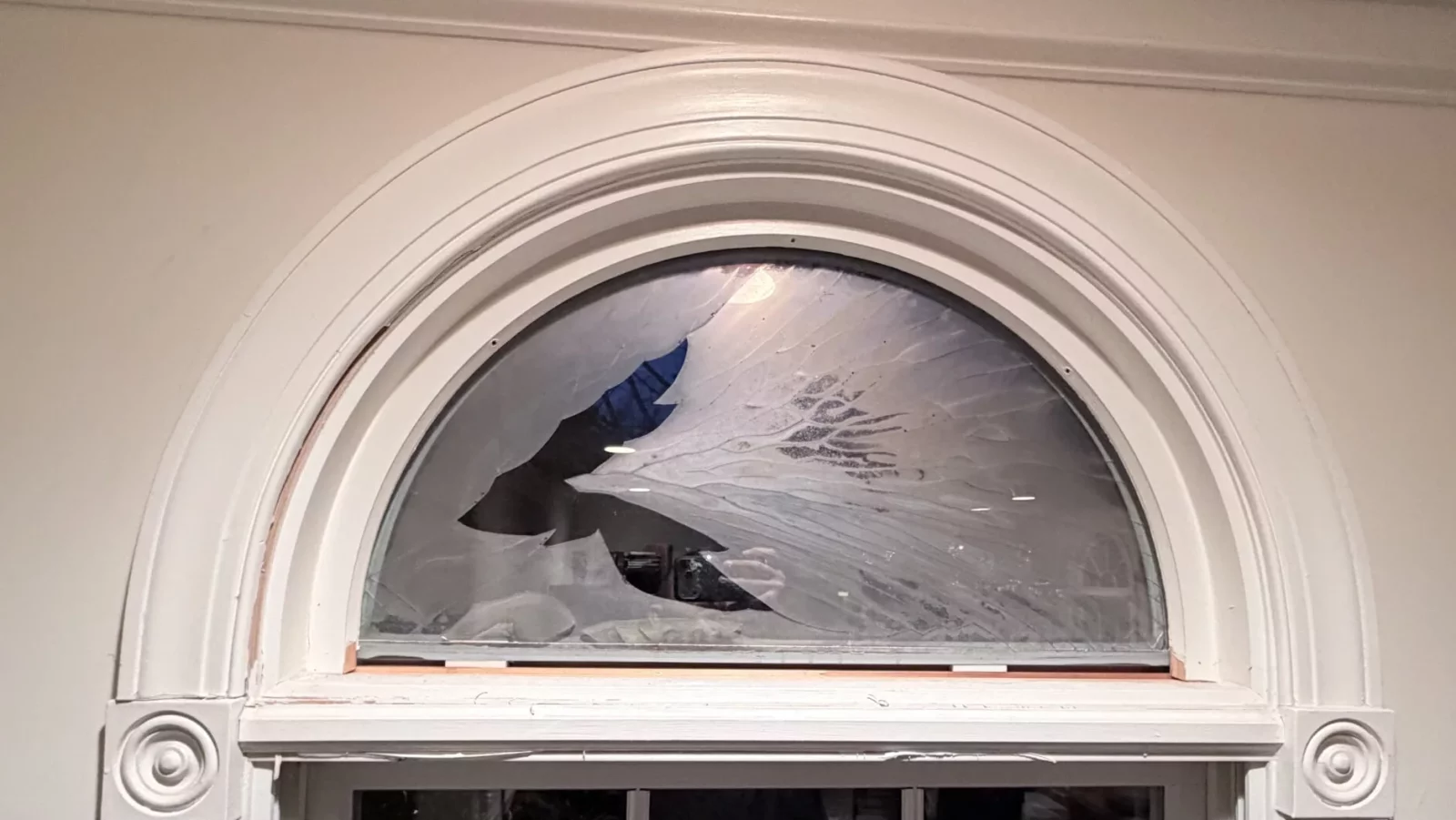 Broken arched window glass above interior window frame