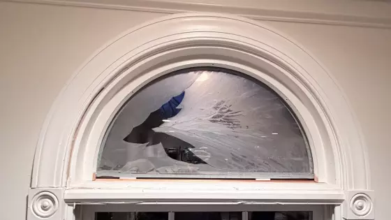 Broken arched window glass above interior window frame