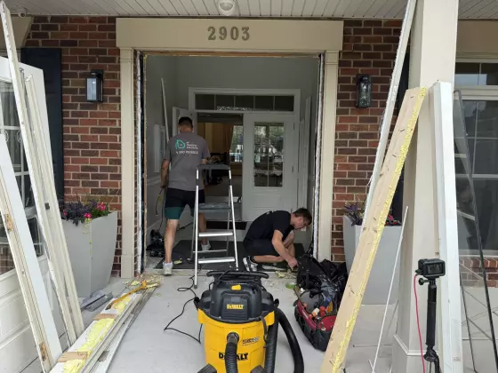 Workers replacing a door at a brick house entrance