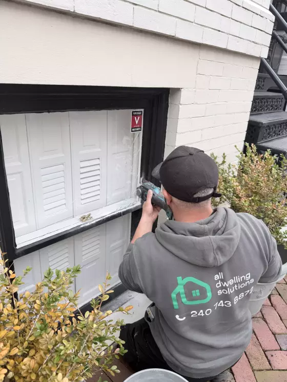 Person using a drill to repair broken window glass on exterior wall