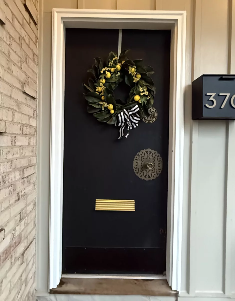Front door with wreath, mailbox, and brick wall visible