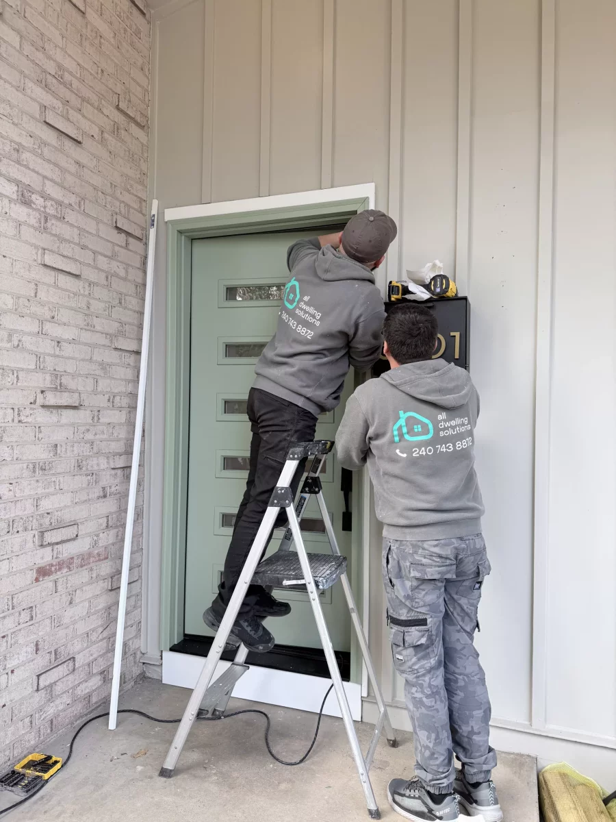 Two workers installing a modern front door with tools and ladder