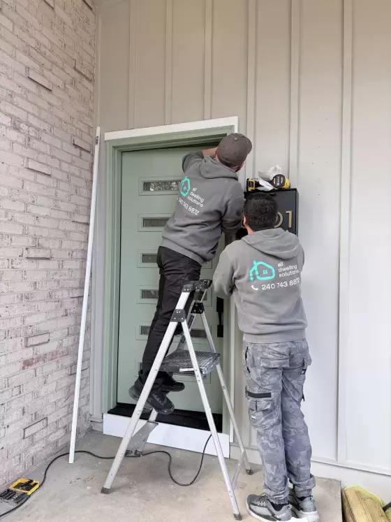 Two workers installing a modern front door with tools and ladder
