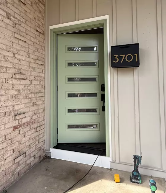 Green entry door being installed with tools visible on porch