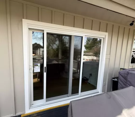 White sliding patio door installed on exterior deck with beige siding