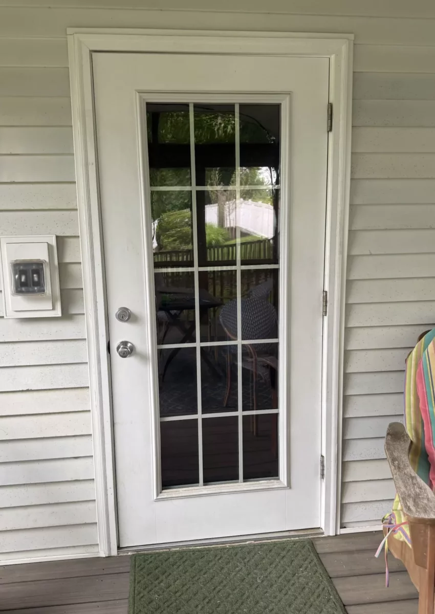 White exterior door with glass panels and green doormat on porch