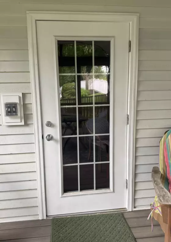 White exterior door with glass panels and green doormat on porch