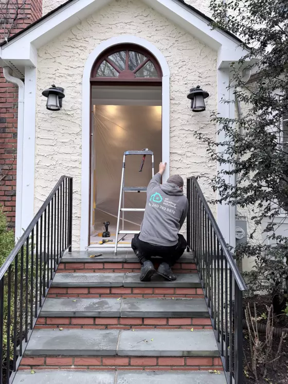 Worker preparing exterior entry door opening with ladder and tools