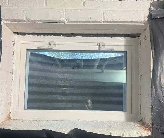 Basement window installation with visible insulation and plastic sheeting