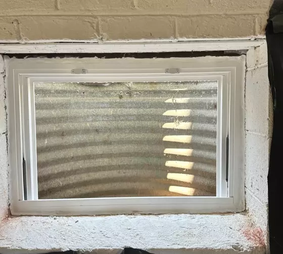 Basement window with white frame set in concrete wall