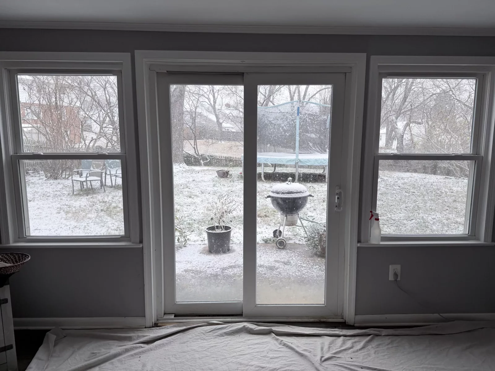 Sliding patio door and windows with drop cloth on floor inside room.