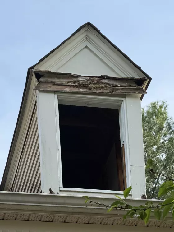 Exterior window opening with visible wood rot and missing window