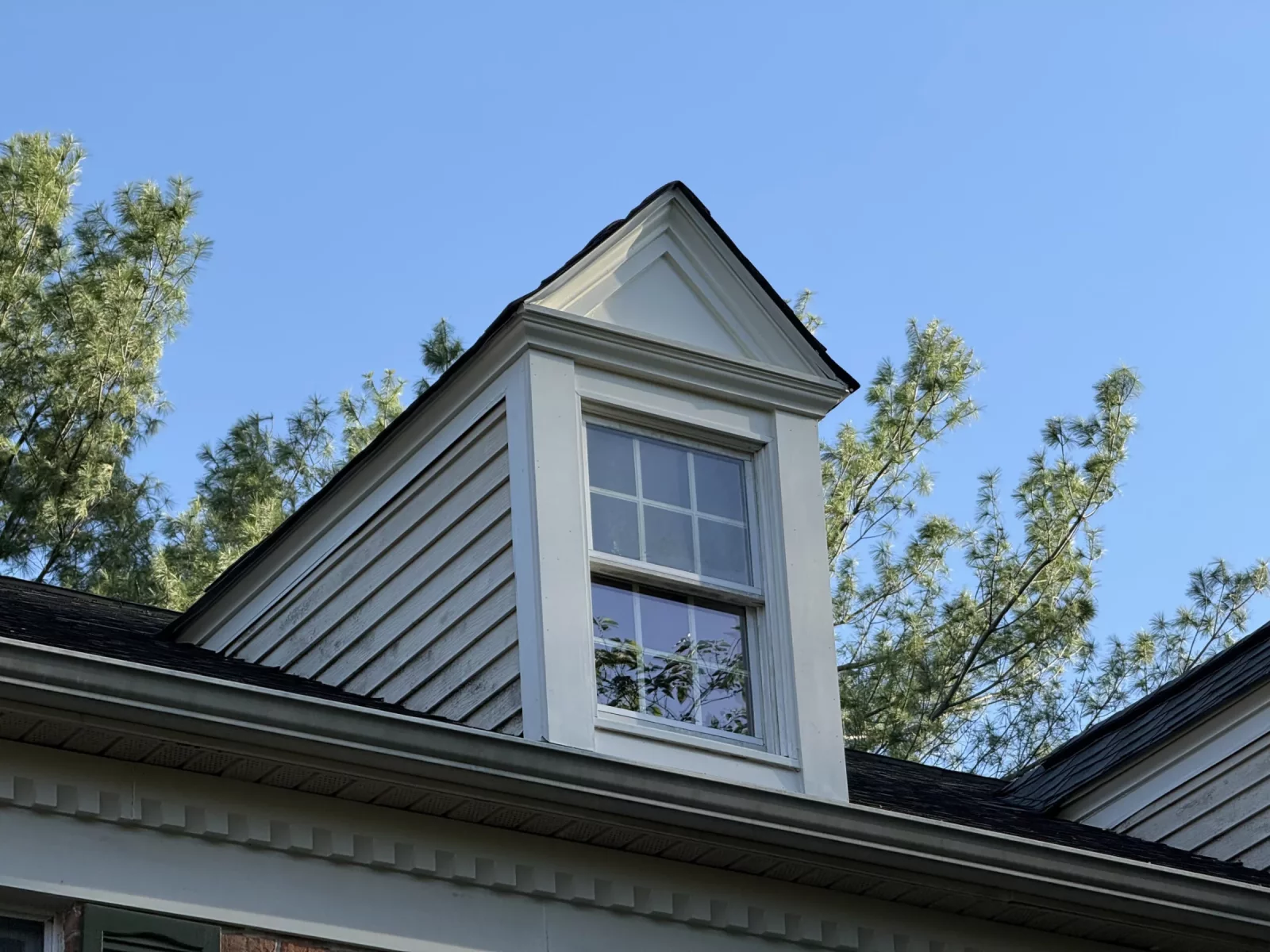 Exterior view of a dormer window with white trim and siding