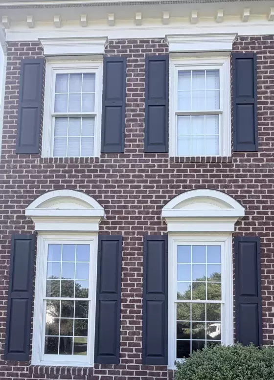 Four windows with black shutters on a brick house exterior
