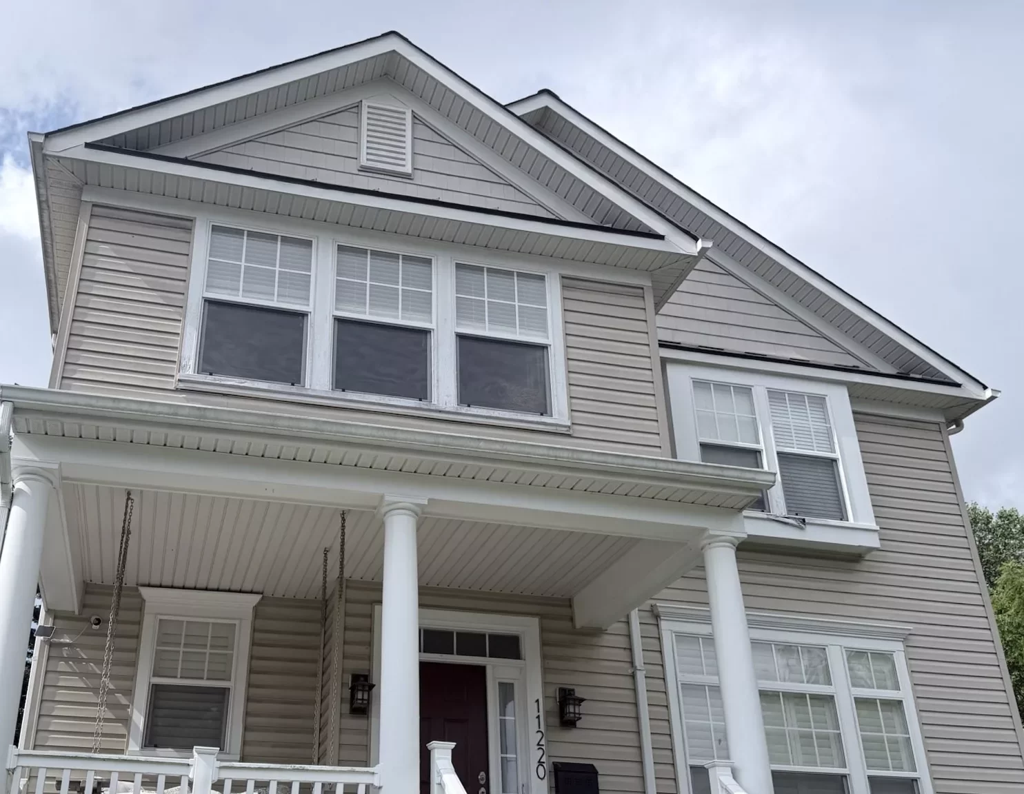 Residential house exterior with beige siding, white trim, and multiple windows