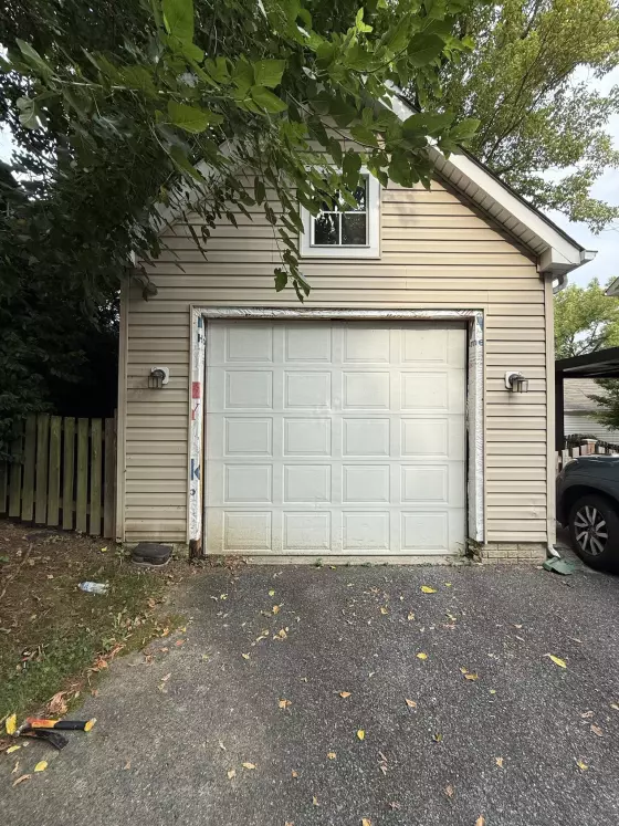 Garage door with exposed trim and tools on driveway