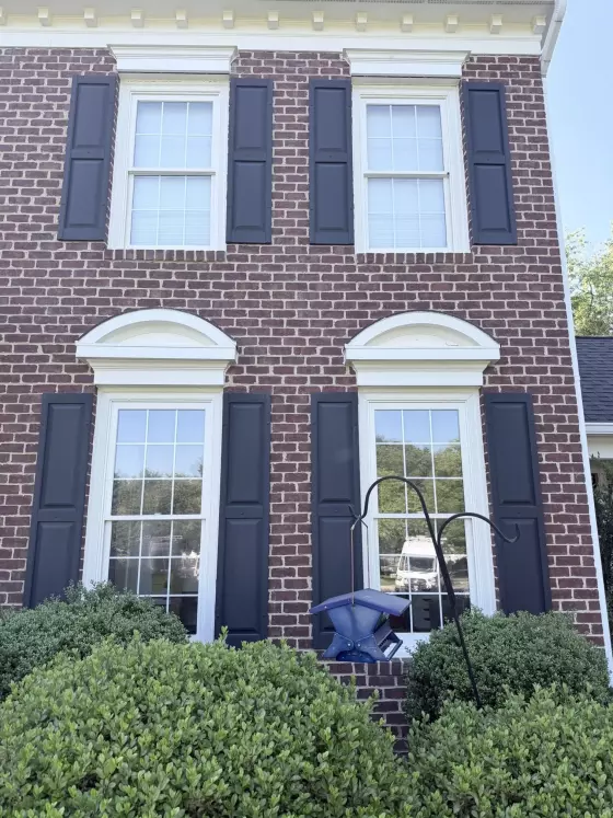 Four windows with black shutters on a brick house exterior