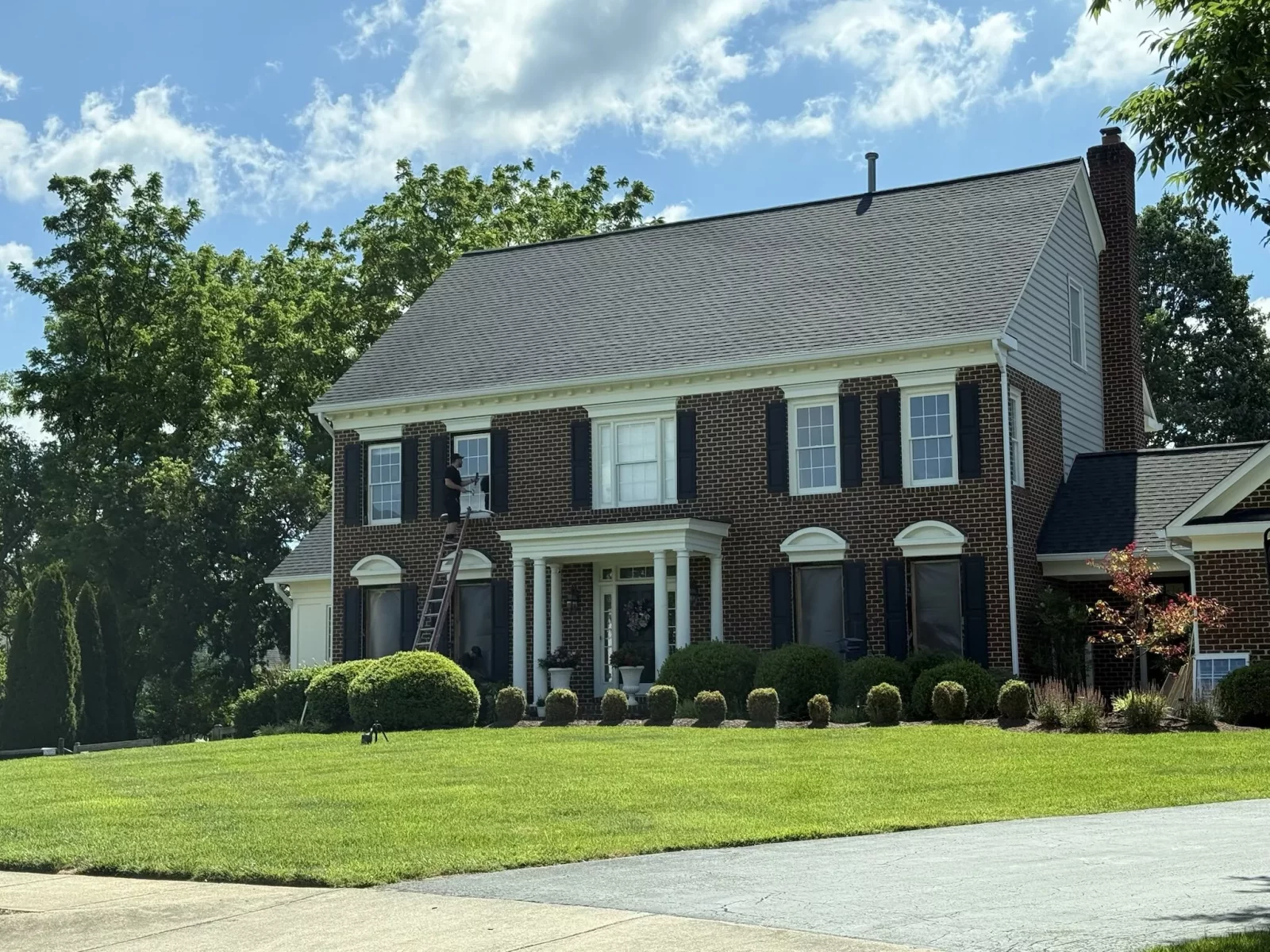 Person on ladder working on window of brick house exterior