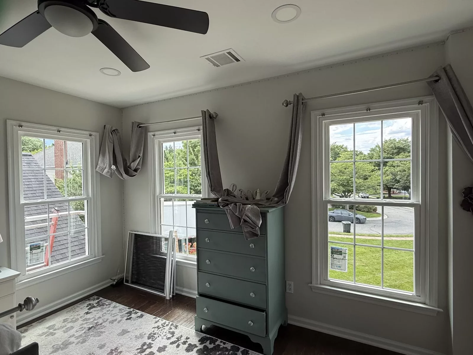 Three double-hung windows in a residential room with screens and dresser visible.