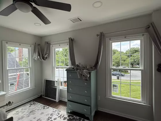 Three double-hung windows in a residential room with screens and dresser visible.
