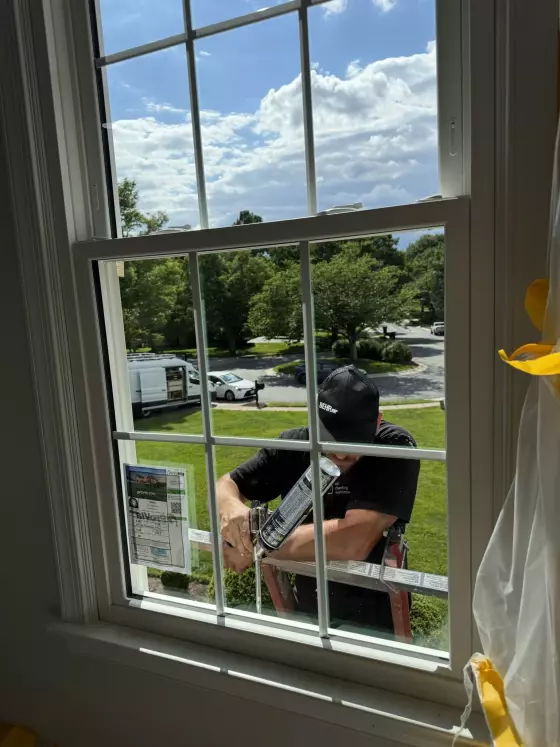 Worker applying caulk to residential window from exterior ladder