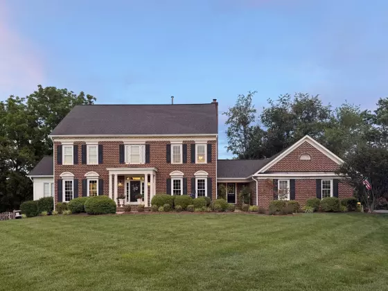 Front view of a brick house with windows, shutters, and a lawn