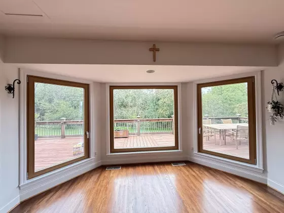 Three large windows with wood trim overlooking a deck and trees