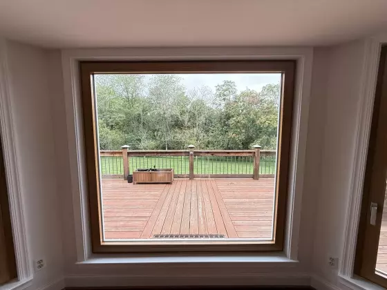 Large window with wood trim overlooking a deck and backyard