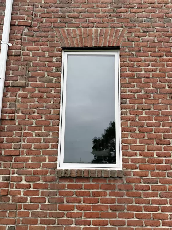 Single window with white frame in red brick exterior wall