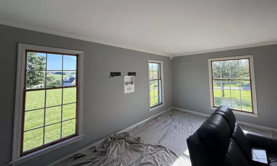 Room with three large windows, gray walls, and drop cloths on the floor